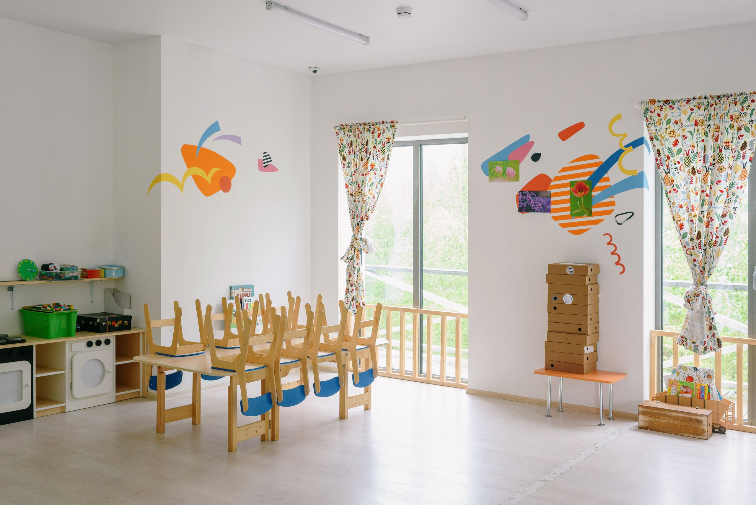 Bright and inviting kindergarten classroom with wooden chairs and playful wall art.