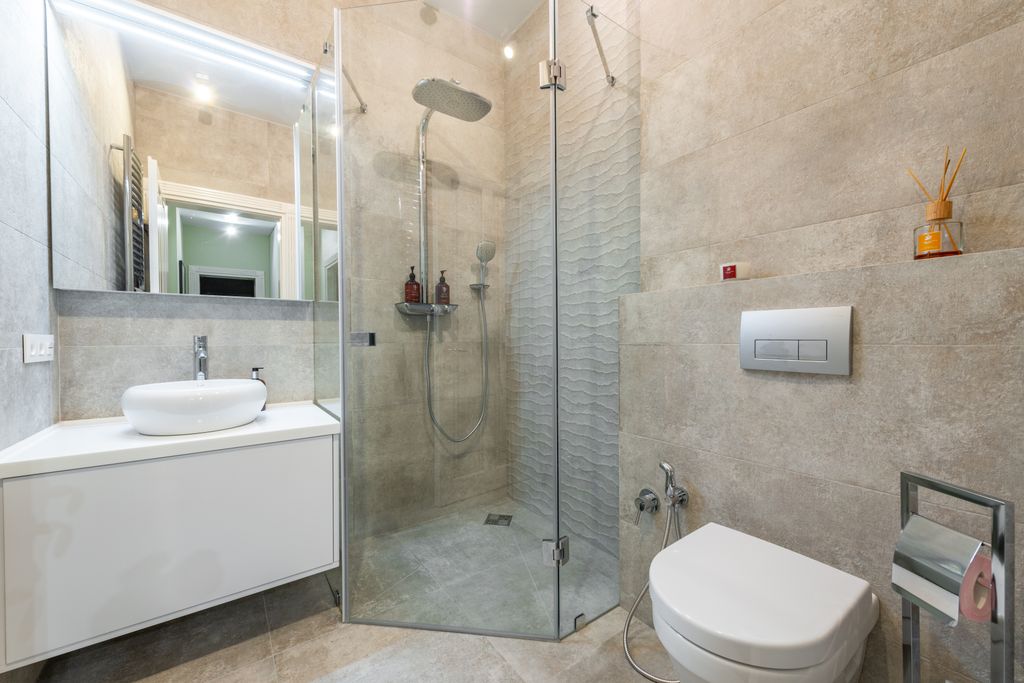 Contemporary shower room between cabinet with washstand and toilet bowl on tiled floor at home