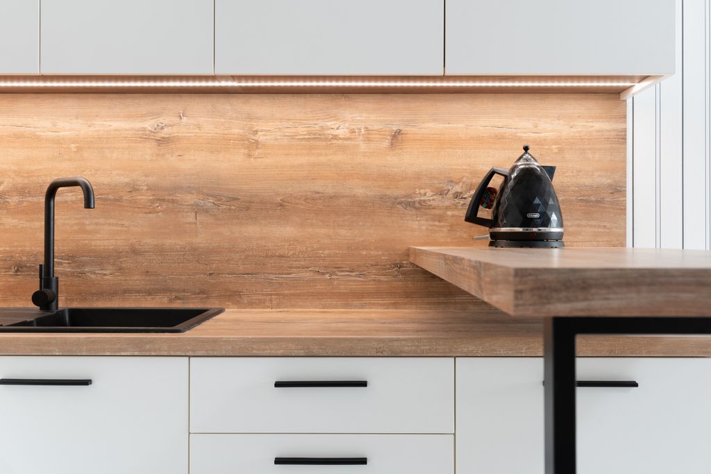 Fragment of interior of contemporary kitchen with white cabinets and wooden details in minimalist style apartment