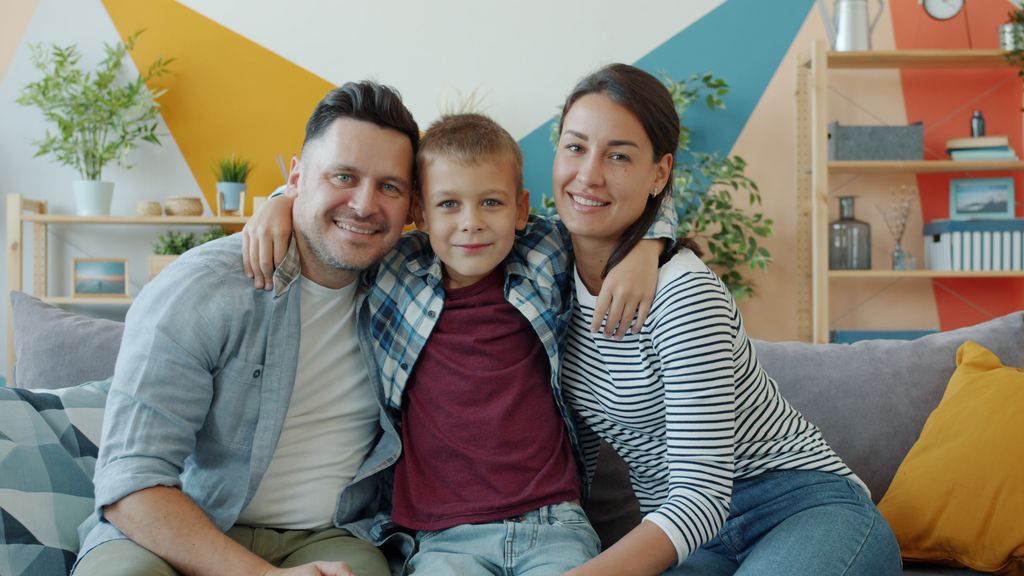 Family portrait of smiling parents and child at home, embracing on a sofa.